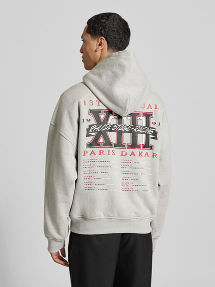 Männermodel trägt Oversized Hoodie aus katoenmix van RHUDE met labelprint, kangoeroezak, ribboorden, ruglengte bij maat M 64 cm, Ganzkörperansicht Rückansicht.