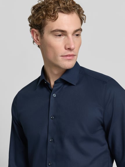 Männermodel trägt Slim Fit Businesshemd mit Kentkragen von OLYMP in Dunkelblau mit feinem Web muster, Nahaufnahme Oberkörper.