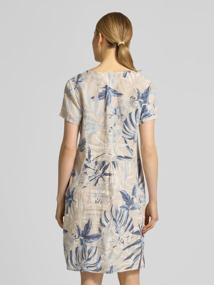 Frauenmodel trägt knielanges Kleid aus Leinen-Mix Modell 'Sa44idaa' von ZABAIONE im Allover-Look mit Rundhalsausschnitt, Gerader-Schnitt, helle Naturtöne mit blauen Blattmotiven, strukturierte Leinen-Baumwoll-Anteil-Oberfläche, Ganzkörperansicht Rückansicht.