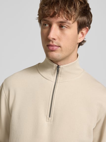Männermodel trägt Regular Fit Sweatshirt mit Troyer-Kragen Modell 'Bradley' von Jack & Jones, beige, glatte Textur, Nahaufnahme Oberkörper. Material-Mix mit Baumwoll-Anteil, elastische Abschlüsse.