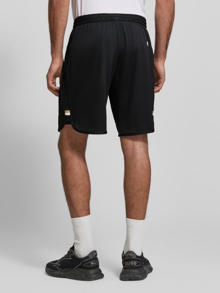 Mannelijk model draagt Regular Fit Shorts met label-opschrift model 'TOC SPIN 9 INCH' van BOSS Green, uni zwart, elastische tailleband, zijzakken, rugaanzicht volledige lichaamsopname.