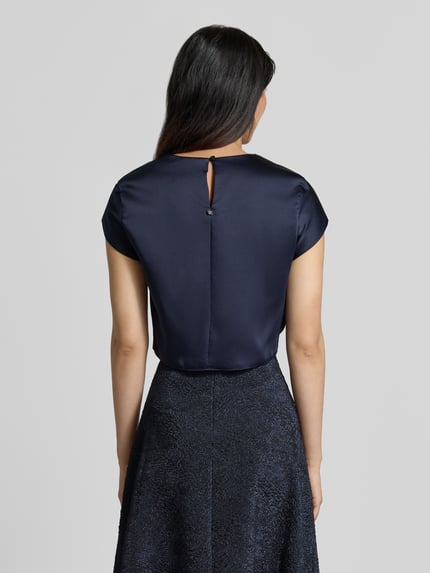 Frauenmodel trägt Bluse aus Satin von Rinascimento, navyblau, gerade Passform, kurzer Ärmel, Rückansicht, Rückseitige Knopfverschluss, Ganzkörperansicht Rückansicht.