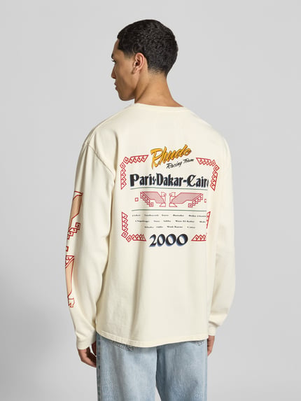 Männermodel trägt Relaxed Fit Longsleeve aus zuiver katoen van RHUDE met labelprint en elastische mouwboorden, ruglengte maat M 70 cm, Ganzkörperansicht Rückansicht.