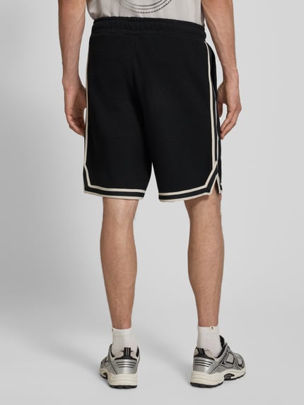 Männermodel trägt Shorts mit Strukturmuster und Label-Stitching von PEGADOR aus reiner Baumwolle, Regular-Fit, Eingrifftaschen, Ganzkörperansicht Rückansicht.