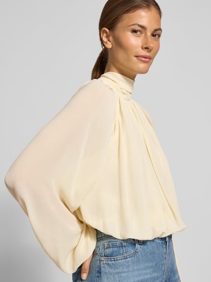 Frauenmodel trägt Regular Fit Bluse mit rückseitiger Schnürung Modell 'NUBE' von MANGO, cremefarben, Strukturmuster, Stehkragen, Raffungen, Nahaufnahme Oberkörper.