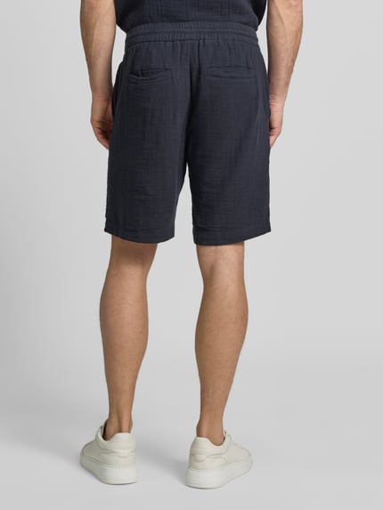 Männermodel trägt Shorts mit Eingrifftaschen und elastischem Bund von Lindbergh in Dunkelblau aus Reine Baumwolle, Loose-Fit, Ganzkörperansicht Rückansicht.