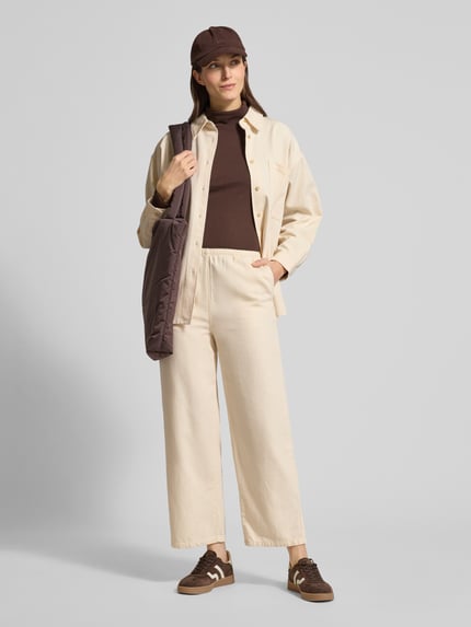 Kobiece modelka nosi Hemdbluse mit Knopfleiste od American Vintage z bawełny w kolorze kremowym, luźny krój, przednie kieszenie, długość tyłu 55 cm, długość rękawa 75 cm; całopostaciowy widok z przodu.