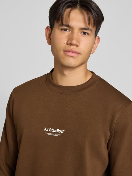 Männermodel trägt Regular Fit Sweatshirt aus Baumwoll-Mix Modell 'Soho' von JACK & JONES, Logo-Print, braun, Nahaufnahme Oberkörper.