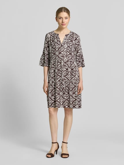 Vrouwenmodel draagt Regular Fit mini-jurk uit zuiver viscose met kachel-print van Christian Berg Woman Selection, getailleerde pasvorm, tuniekhals en halflange mouwen, ruglengte maat 36: 89 cm, borstwijdte: 46 cm, mouwlengte: 39 cm, zwart-witte tinten, geometrische vormen, gladde textuur, geheelopname van voren.