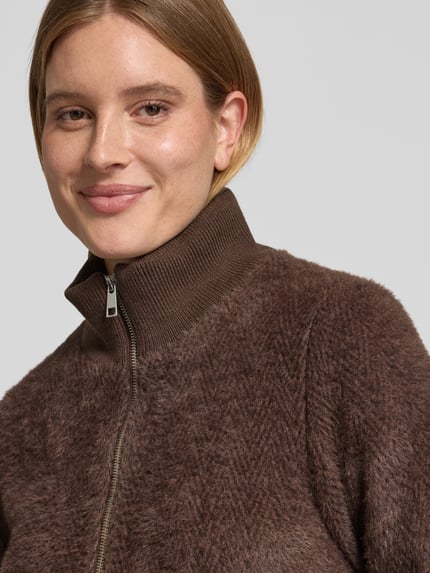 Frauenmodel trägt Mantel mit Stehkragen und Reißverschluss Modell 'An44astasia' von ZABAIONE, braune Textur, Nahaufnahme Oberkörper.