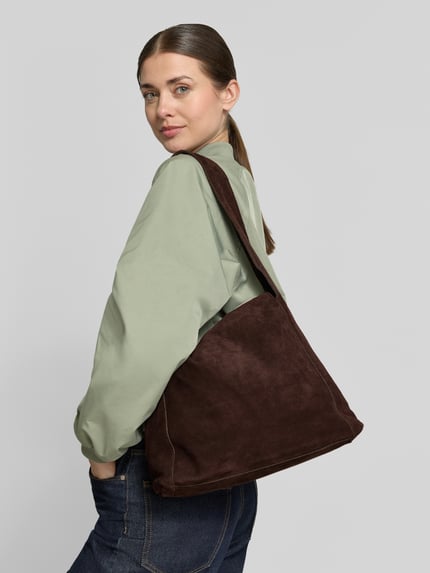 Frauenmodel trägt dunkelbraune Handtasche aus Rindsleder Modell 'PIRAMIDE' von Mango mit breitem Schulterriemen, Ganzkörperansicht Rückansicht.