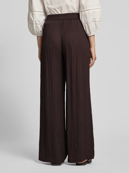 Frauenmodel trägt Wide-Leg-Pants aus Reine Viskose mit elastischem Bund von Someday, dunkelbraun, Loose-Fit, Ganzkörperansicht Rückansicht. Modell 'Cenya resort', Bundweite bei Größe 36: 39 cm, Innenbeinlänge: 81 cm.
