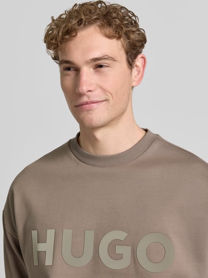 Männermodel trägt Oversized Sweatshirt aus reiner Baumwolle Modell 'DINEX' von HUGO in Optik: Unifarben mit Label-Print, Nahaufnahme Oberkörper.