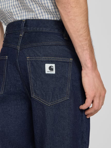 Männermodel trägt Wide Fit jeans uit puur katoen Model "Brandon" van Carhartt Work In Progress, 5-pocketmodel, riemlussen, knoop- en ritssluiting, bandwijdte maat S 41 cm, binnenbeenlengte maat S 73 cm, detailaufnahme rug, KI-modifiziertes Bild