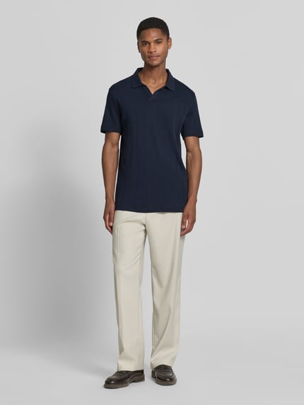 Männermodel trägt Regular Fit Poloshirt in Jaquard-Strick von Lindbergh, Reine Baumwolle, Polokragen, V-Ausschnitt, Label-Detail, Ganzkörperansicht von vorne.