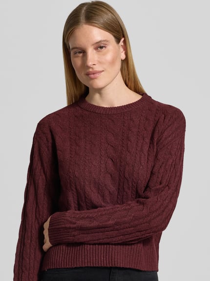 Frauenmodel trägt unifarbenen Pullover mit Zopfmuster Modell 'VMSEQUOIA' von VERO MODA, Crew Neck, Stricktextur, Nahaufnahme Oberkörper.