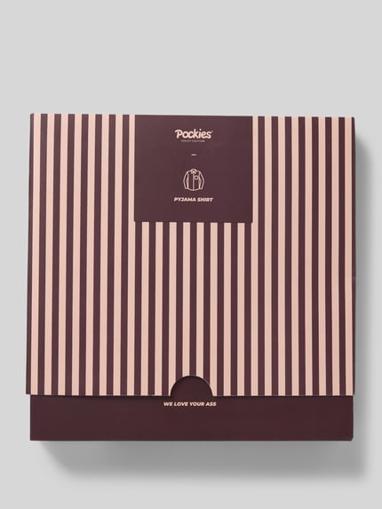 Produktfoto, Verpackung des Pyjama-Oberteil mit Brusttasche von POCKIES, dunkelviolette und rosafarbene Streifen auf Karton, rechteckige Form.