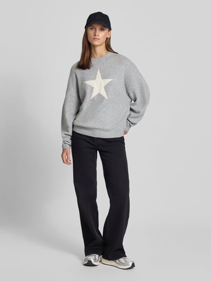 Frauenmodel trägt Regular Fit Pullover in Strick-Optik von REVIEW, grau mit weißem Stern, Langarm, gerippte Abschlüsse, Ganzkörperansicht von vorne.