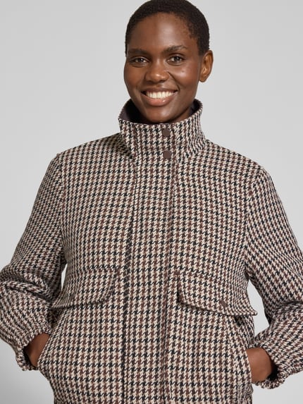 Frauenmodel trägt Bomberjacke mit Stehkragen Modell 'VMCHERYL' von VERO MODA im Hahnentritt-Allover-Muster mit elastischen Abschlüssen, Nahaufnahme Oberkörper.