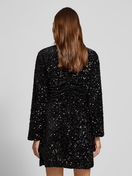 Frauenmodel trägt Minikleid mit Pailletten Modell 'BARINA' von Vila in Schwarz, Struktur durch Pailletten, A-Linie, Ganzkörperansicht Rückansicht.