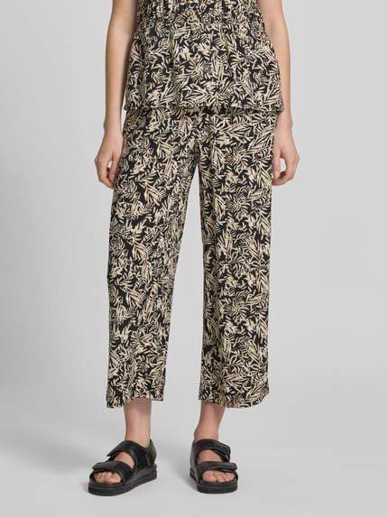 Frauenmodel trägt Straight Fit Stoffhose aus reiner Viskose-Mix Modell 'Faye' von Soyaconcept mit floraler Allover-Print, verkürzte Passform und elastischem Bund mit Tunnelzug, Farbe Beige und Schwarz, glatte Textur, Damen Stoffhose, Ganzkörperansicht von vorne.