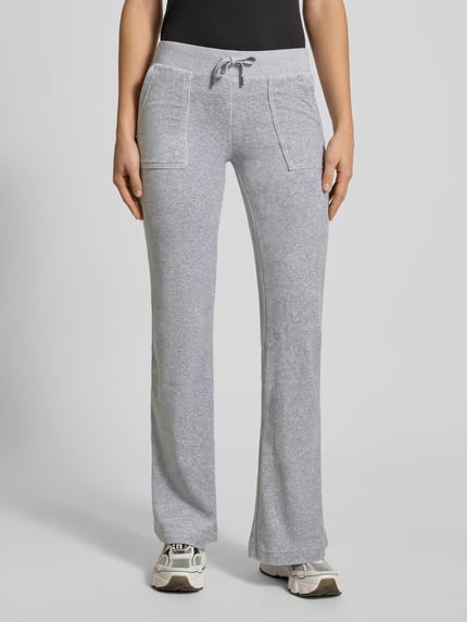 Frauenmodel trägt Low Rise Sweatpants mit elastischem Bund Modell 'LAYLA' von Juicy Couture aus grauem Baumwoll-Mix mit Stretch-Anteil, Flared-Cut, Eingrifftaschen, Innenbeinlänge 39 cm, Ganzkörperansicht von vorne.