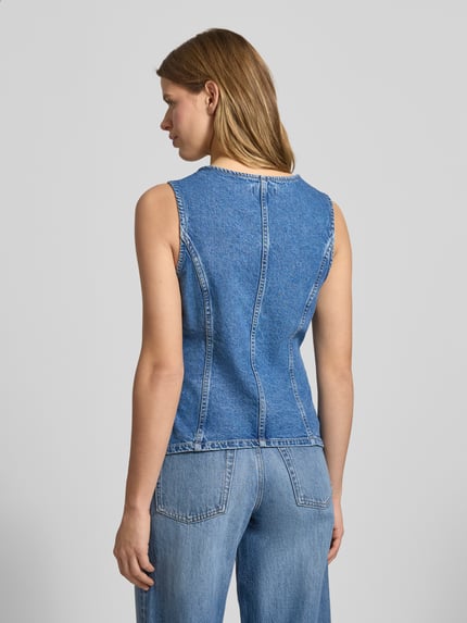 Frauenmodel trägt Jeansweste aus reiner Baumwolle Modell 'GUILINA' von ONLY in blauer Denim-Optik mit Paspeltaschen, Ganzkörperansicht Rückansicht.