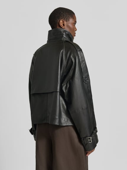 Frauenmodel trägt schwarze Regular Fit Jacke in Leder-Optik Modell 'Zavic' von Gestuz mit Stehkragen und doppelter Knopfleiste, Ganzkörperansicht Rückansicht.