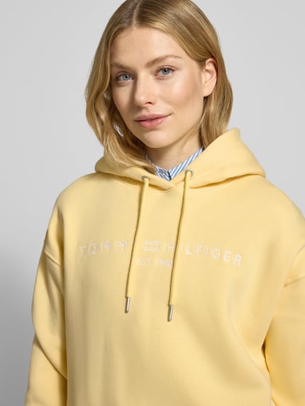 Vrouwenmodel draagt Relaxed Fit Hoodie aus Baumwoll-Mix van Tommy Hilfiger, effen geel, label stitching, katoenmix sweatstof, Nahaufnahme bovenlichaam.