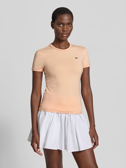 Frauenmodel trägt Slim Fit T-Shirt aus Baumwoll-Mix von Lacoste in Apricot, unifarben, Logo-Stitching, Kontrastpaspel, Ganzkörperansicht von vorne.