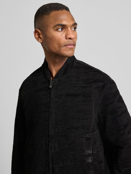 Männermodel trägt Bomberjacke mit Reißverschluss von ARMANI EXCHANGE in Schwarz, Material-Mix mit Stretch-Anteil, Nahaufnahme Oberkörper.