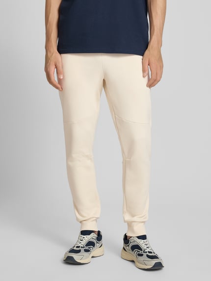 Männermodel trägt Regular Fit Sweatpants mit Label-Applikation von Balr. in Beige aus Baumwoll-Mix, Ganzkörperansicht von vorne.