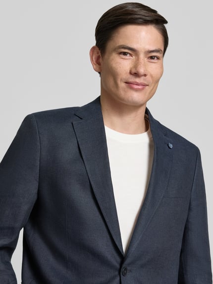 Männermodel trägt Regular Fit Sakko aus reinen Leinen mit Reverskragen von Christian Berg Men in Dunkelblau mit Brusttasche, AufgesetzteTaschen und 2-Knopfleiste, Nahaufnahme Oberkörper. Rückenlänge bei Größe 50: 75 cm, Schulterbreite: 47 cm, Ärmellänge: 63 cm.