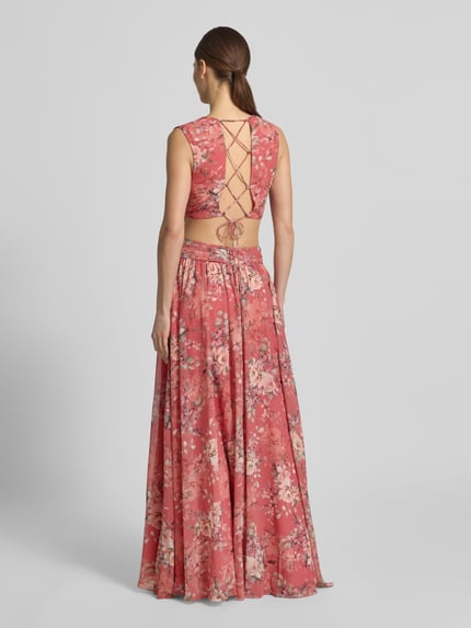 Modelka nosi Regular Fit Maxikleid mit floralem Allover-Print von ADLYSH, odcień różowy, kwiatowy nadruk na całej powierzchni, plisy, dekolt w serek, krój bez rękawów, obszycie falbanami, wycięcia, wiązanie, długość tyłu w rozmiarze S: 52 cm, szerokość w rozmiarze S: 32 cm, widok całej sylwetki z tyłu.