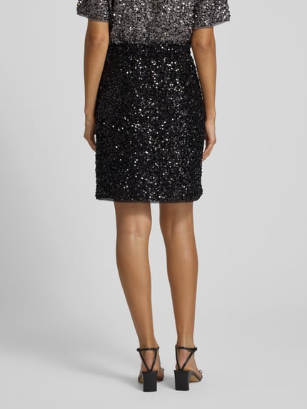 Frauenmodel trägt Minirock mit Pailletten und elastischem Bund von comma, gerader Schnitt, schwarze Glitzerstruktur, Ganzkörperansicht Rückansicht.