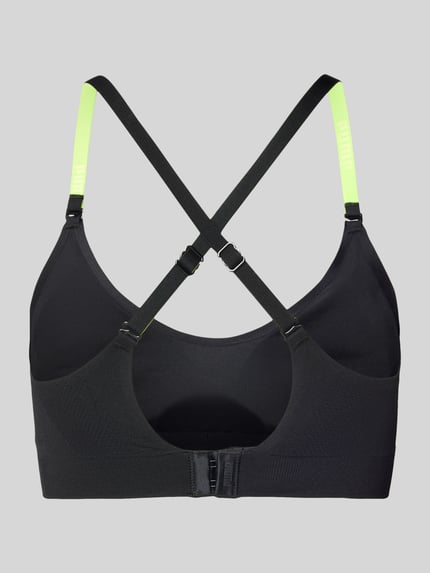 Frauenmodel trägt Triangel-BH mit Logo und gekreuzten Trägern von PUMA, Schwarz mit neongelben Verstellbarer-Trägern, Material-Mix mit Stretch-Anteil, Hakenverschluss, Körpernahe Passform, Ganzkörperansicht Rückansicht.