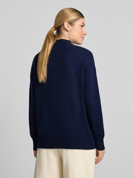 Frauenmodel trägt Strickpullover aus Kaschmir-Mix mit Woll-Anteil Modell 'Nina' von 0039 Italy in Dunkelblau, Ganzkörperansicht Rückansicht. Regular Fit, überschnittene Schultern, gerippte Abschlüsse, gerippter Stehkragen, Strick-Optik, Rückenlänge 56 cm, Ärmellänge 46 cm.
