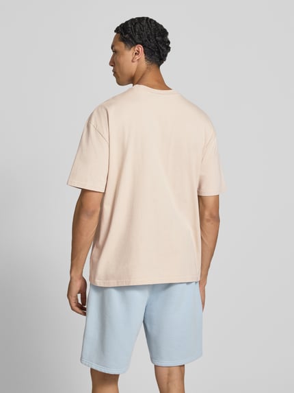 Männermodel trägt Oversized T-Shirt mit Label-Stitching von Pegador aus Baumwoll-Mix in Beige mit Rundhalsausschnitt, Rückenlänge 70 cm, Ganzkörperansicht Rückansicht.