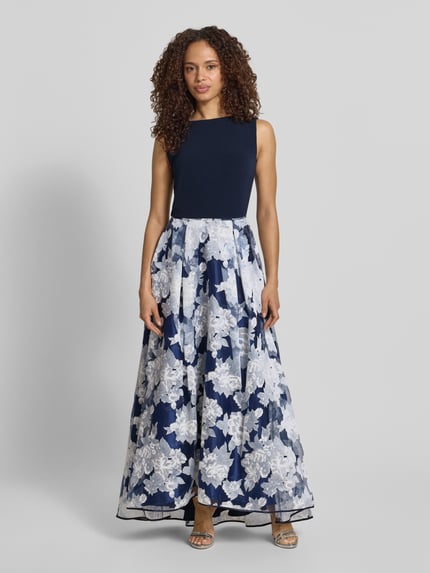 Kobieta modelka nosi 'Abendkleid mit rückseitigem V-Ausschnitt' od Christian Berg Cocktail, granatowy góra, biało-niebieska spódnica w kwiaty, materiał z domieszką stretchu, krój taliowany, długość maxi, dekolt łódkowy, zamek z tyłu, długość tyłu w rozmiarze 36: 130 cm, szerokość w rozmiarze 36: 47 cm, widok całej sylwetki z przodu.
