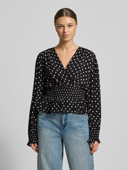 Vrouwenmodel draagt Blouse uit zuivere viscose in wikkellook Model 'Tamona' van Neo Noir, regular fit, met lange mouwen, V-hals, getailleerde pasvorm, ruches, ruglengte maat 36: 58 cm, mouwlengte maat 36: 66 cm, zwart met witte stippen, vooraanzicht bovenlichaam.
