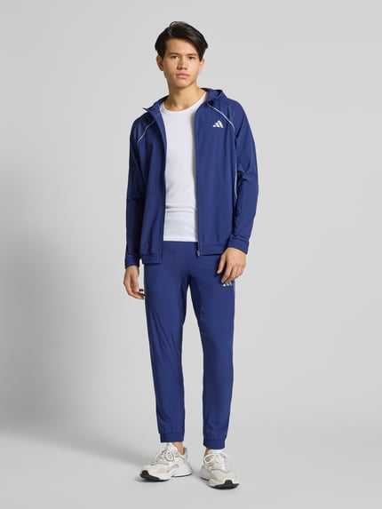 Männermodel draagt Slim Fit Sweatpants met Logoprint Model 'Tech' van adidas Training in blauw, elastische materiaalmix, Ganzkörperansicht von vorne.