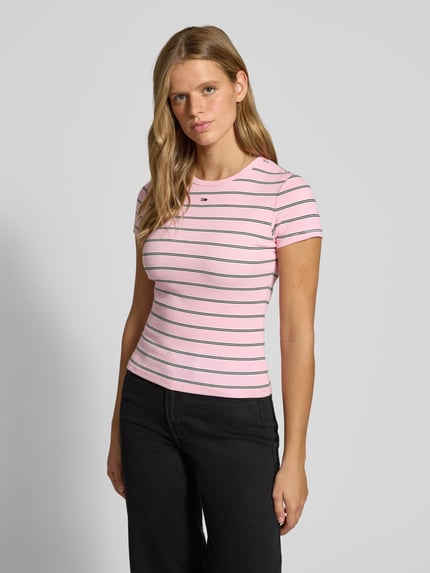 Frauenmodel trägt Slim Fit T-Shirt aus Baumwoll-Mix von Tommy Jeans in Rosa mit schwarzen Streifen, glatte Struktur, Nahaufnahme Oberkörper. Damen T-Shirt von Tommy Jeans.