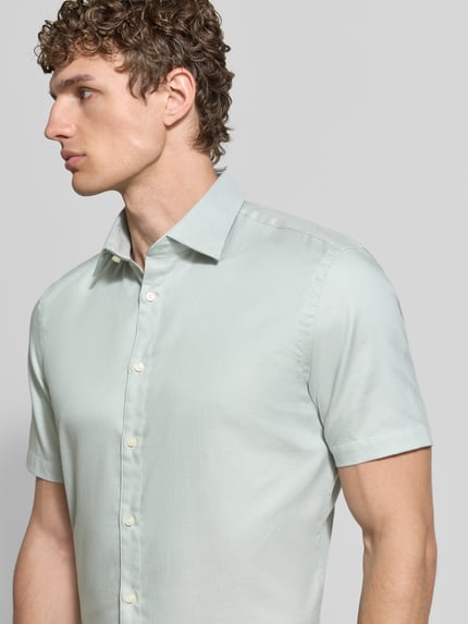 Männermodel trägt Slim Fit Business-Hemd aus Baumwolle mit Kentkragen von Jake*s in hellem Pastellgrün, glatte Textur, Nahaufnahme Oberkörper. Schulterbreite 47 cm, Ärmel 24 cm, Rückenlänge 78 cm bei Größe 39/40.