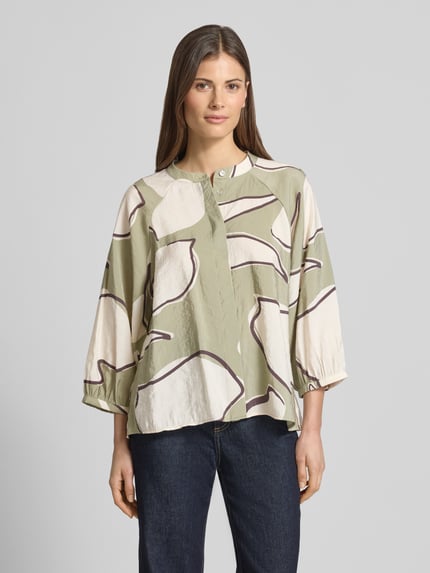 Modelka nosi Bluse mit Rundhalsausschnitt Modell 'Faloom' von OPUS, modal-mix, krój loose fit, z zakrytą listwą guzikową, rękaw 3/4, długość pleców 63 cm, długość rękawa 45 cm, wzór beżowo-oliwkowy z ciemnymi liniami, widok całej sylwetki z przodu.