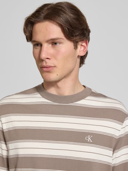 Mannelijk model draagt Regular Fit T-shirt uit katoenmix van Calvin Klein Jeans met all-over gestreept motief, logostitching, ronde hals, korte mouw, close-up bovenlichaam.