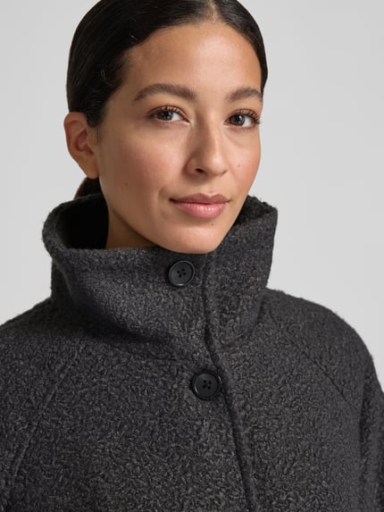 Frauenmodel trägt Teddymantel mit hohem Stehkragen von TOM TAILOR in Anthrazit, reine Polyesterstruktur, Knopfleiste, Nahaufnahme Oberkörper.