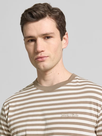 Männermodel trägt Regular Fit T-Shirt aus reiner Baumwolle von Marc O'Polo mit beigem und weißem Allover-Streifenmuster, Nahaufnahme Oberkörper.