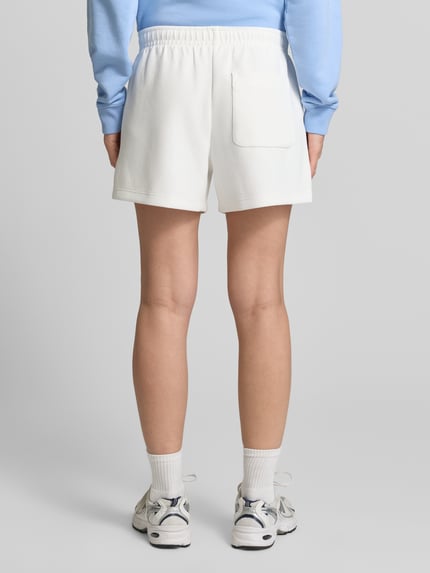 Frauenmodel trägt Regular Fit Sweatshorts aus reiner Baumwolle von Lacoste in Unifarben mit elastischem Bund und Logo-Stitching, Ganzkörperansicht Rückansicht.