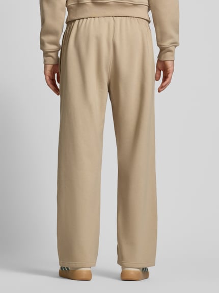 Männermodel trägt Wide Fit Sweatpants mit elastischem Bund von adidas Originals in Beige, Baumwoll-Mix, Logo-Stitching, Ganzkörperansicht Rückansicht.