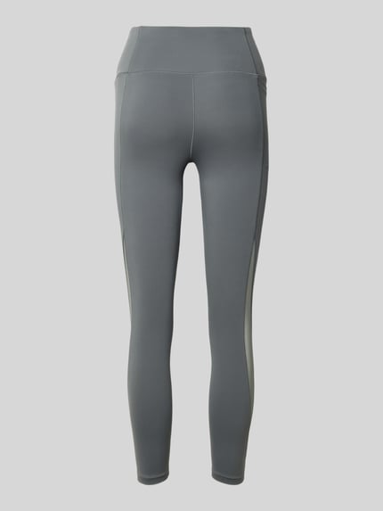 Produktfoto, Slim Fit Leggins mit semitransparenten Partien Modell 'Motion' von Under Armour, elastyczna mieszanka materiałów, krój slim fit, półprzezroczyste części, kieszeń na nogawce, szeroki pas, nadruk z logo, skrócona długość, kolor szary, gładka tekstura, kontrastujące wstawki